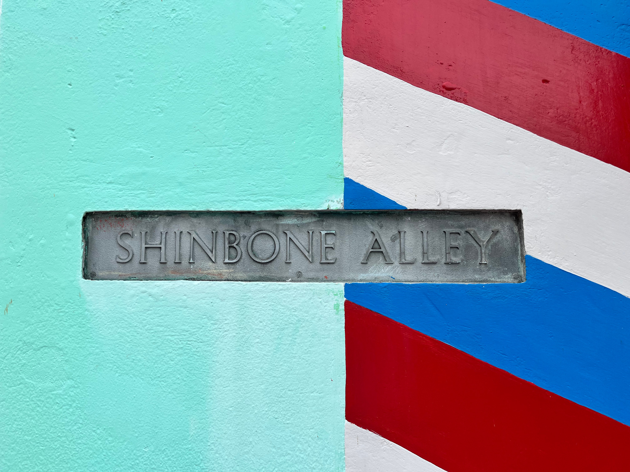 Shinbone Alley sign on a turquoise wall with red and blue stripes